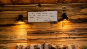 Ein gemütliches Schlafzimmer mit einer Wand aus Holzstämmen, einem Bett mit gemusterten Textilien, einem Nachttisch mit Lampe und einem Tablett mit Frühstücksgebäck.