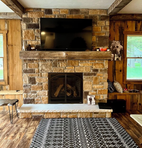 A stone fireplace with a flat-screen TV above it, a mantel with decorative items, and a patterned rug on the floor.