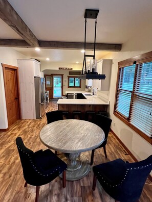 A kitchen with a central island, a dining table with chairs, wooden flooring, and a hanging light fixture.