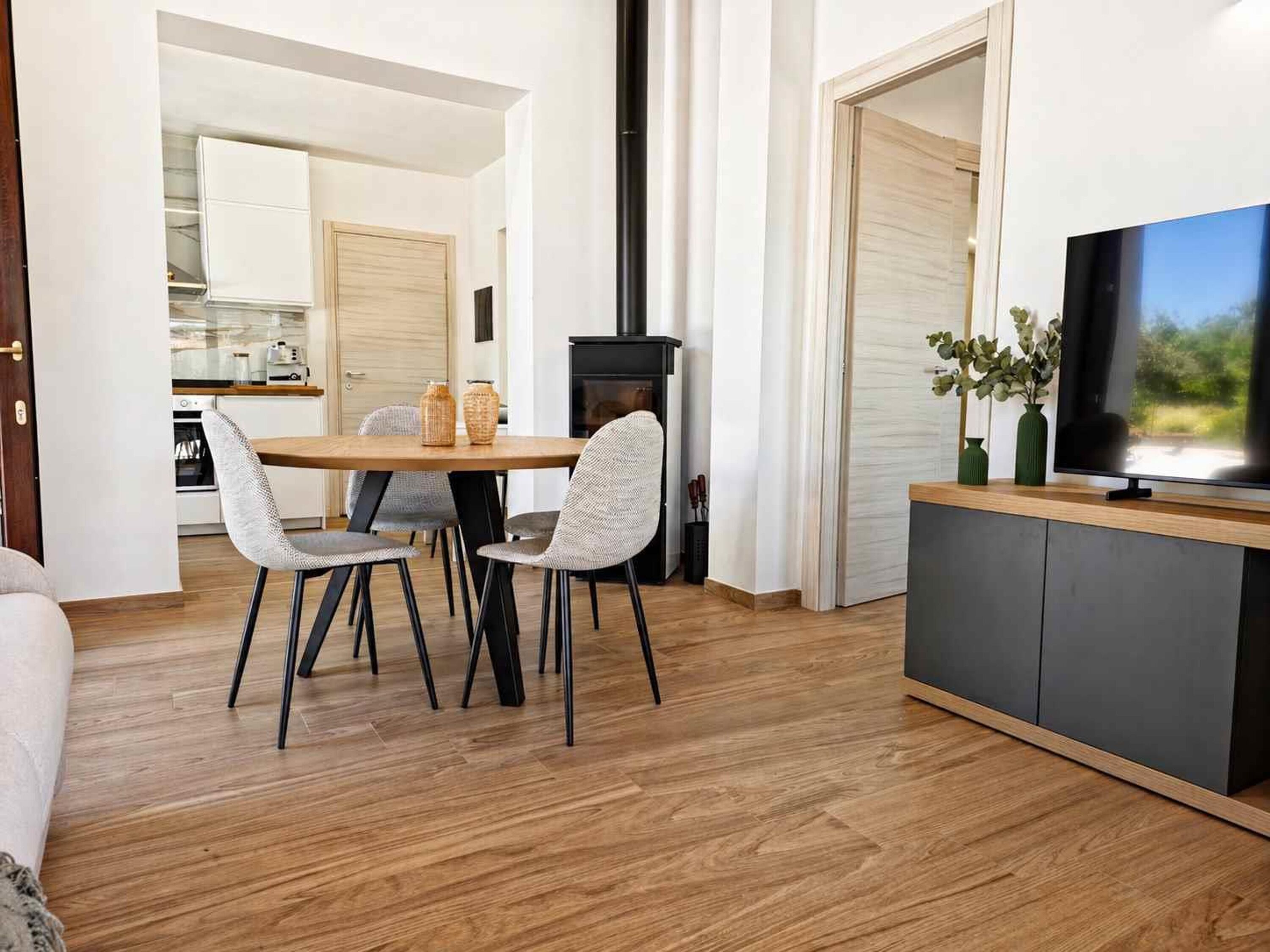 Una sala moderna con comedor, televisor y cocina al fondo.