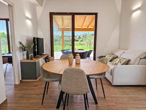 Ein modernes Wohnzimmer mit Essbereich, Fernseher und Blick auf einen Garten durch große Schiebetüren.