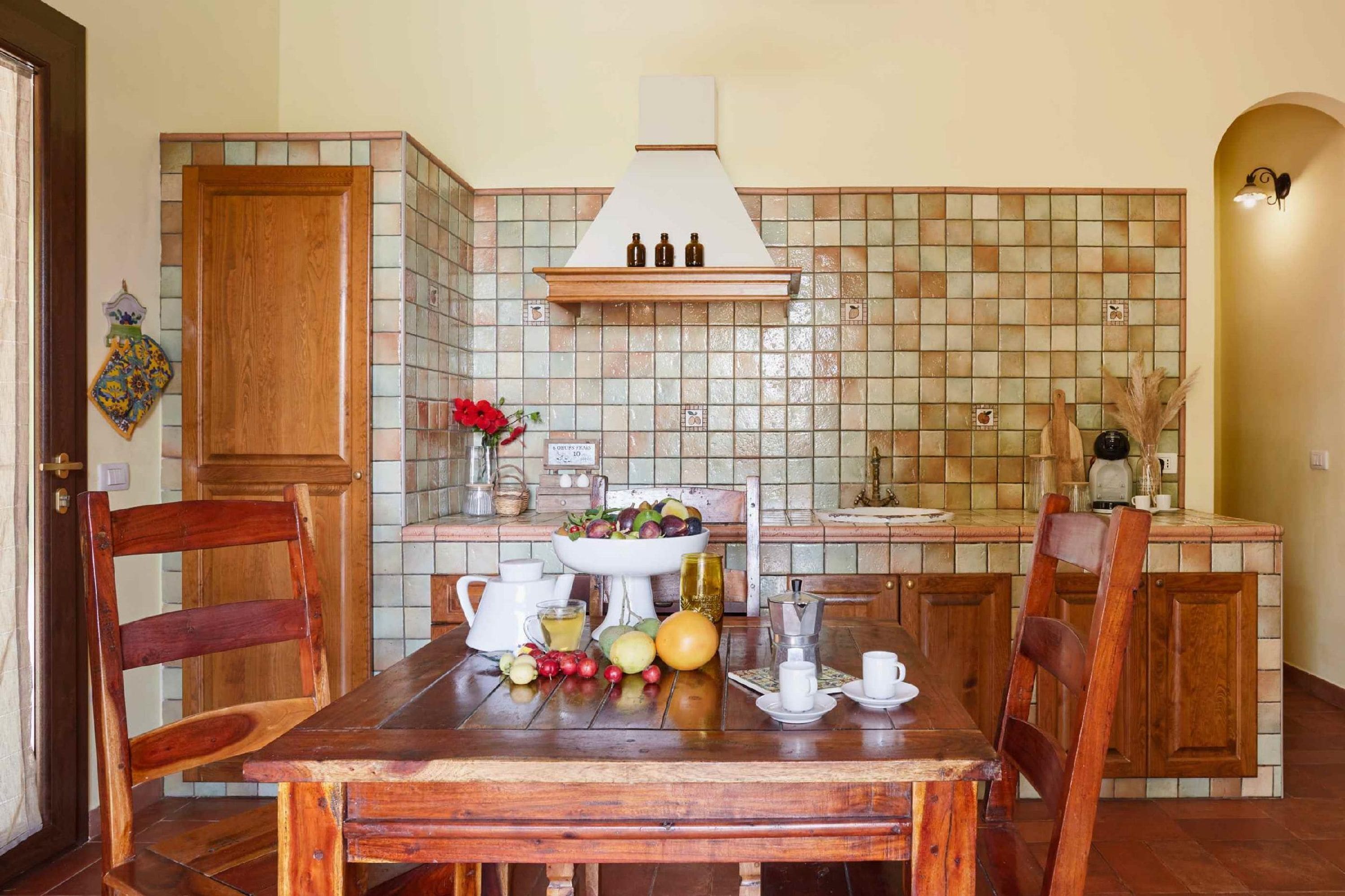 Una cocina con salpicadero de azulejos, armarios de madera, una isla central y una mesa de comedor con frutas y una cafetera.