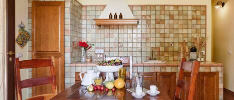 Una cocina con salpicadero de azulejos, armarios de madera, una isla central y una mesa de comedor con frutas y una cafetera.