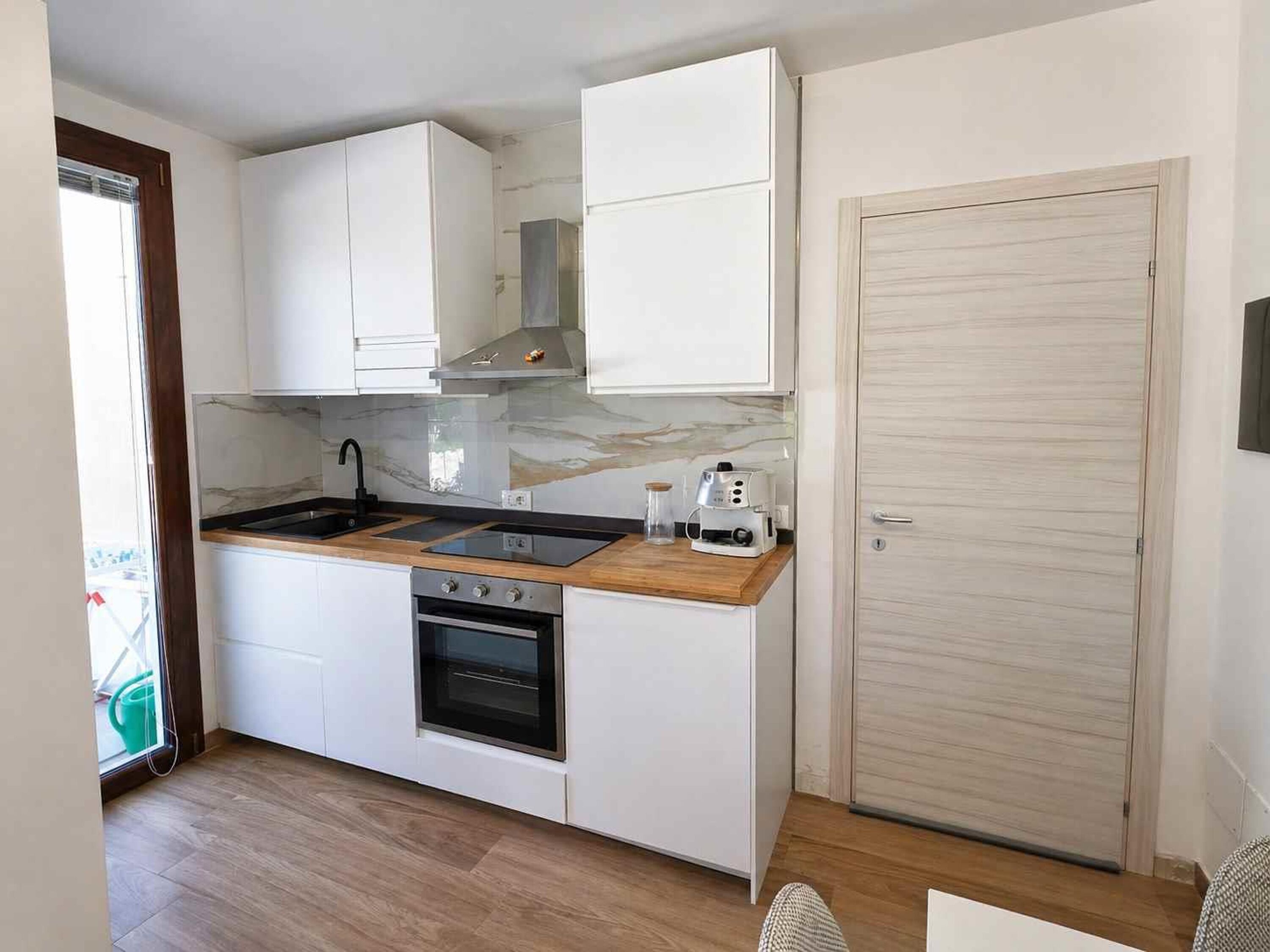 Una cocina compacta con armarios blancos, encimera de madera, horno empotrado y cafetera.