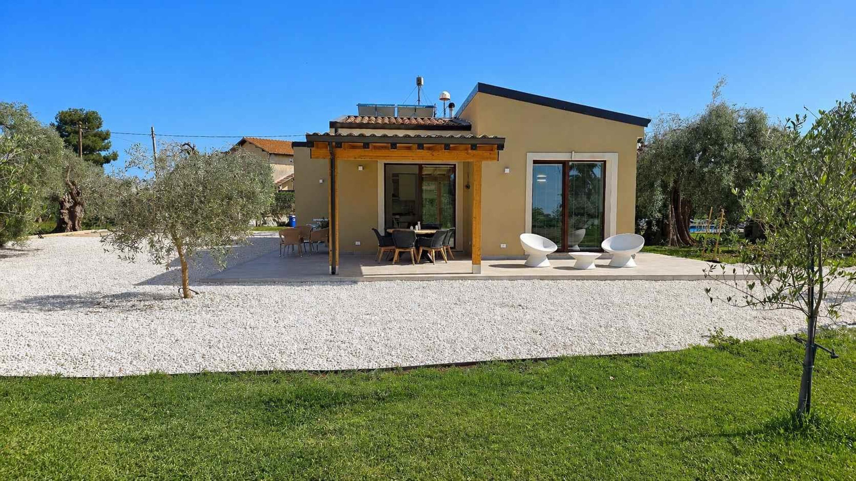 A modern house with a patio, outdoor seating, and a gravel driveway.