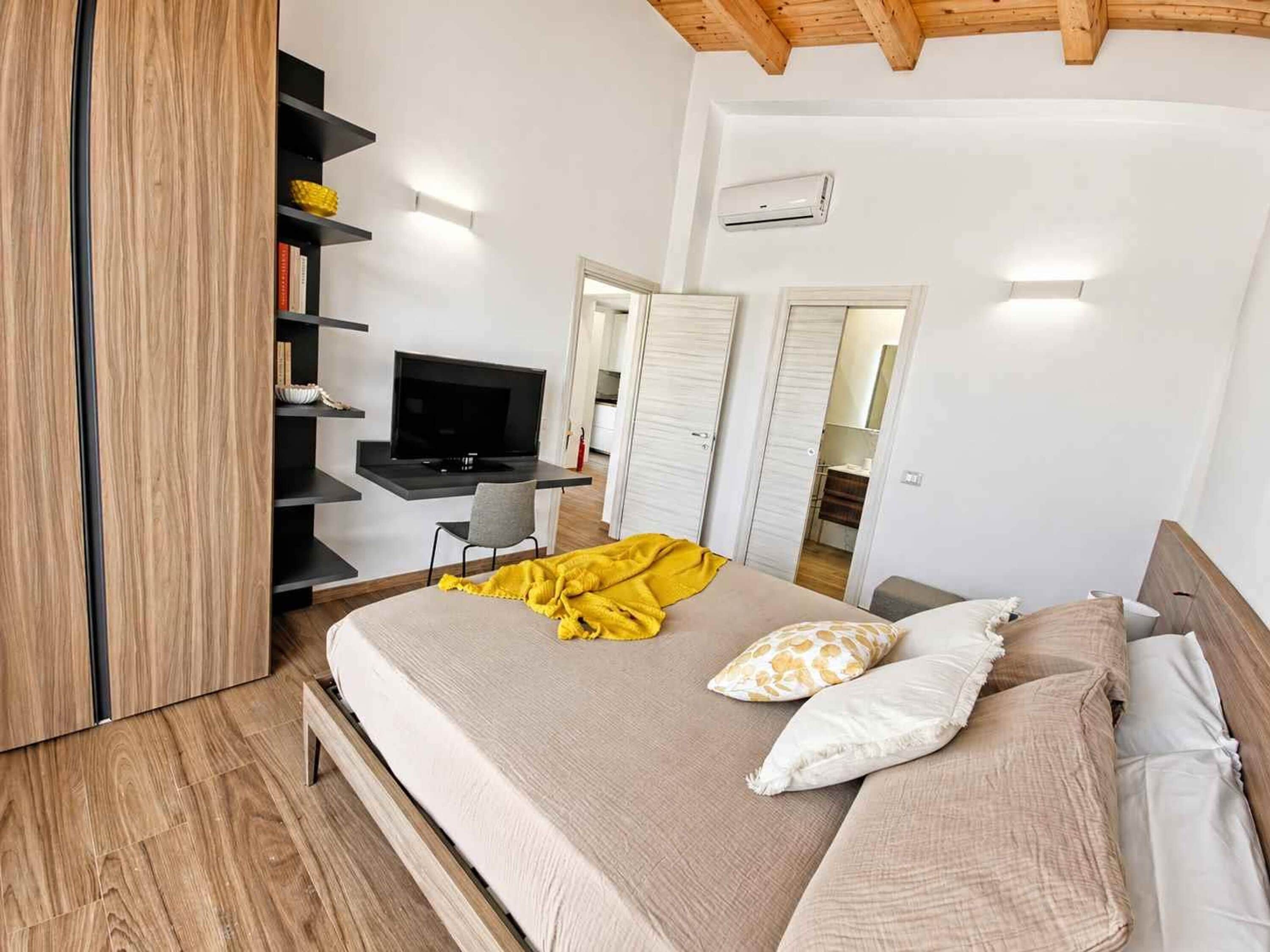 Un dormitorio con cama, televisor, armario y escritorio.