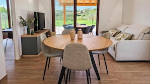 Een moderne woonkamer met een eethoek, een televisie en uitzicht op een tuin door grote schuifdeuren.
