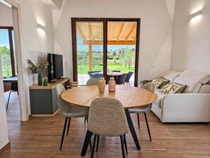 Una sala de estar moderna con comedor, televisor y vista a un jardín a través de amplios ventanales correderos.