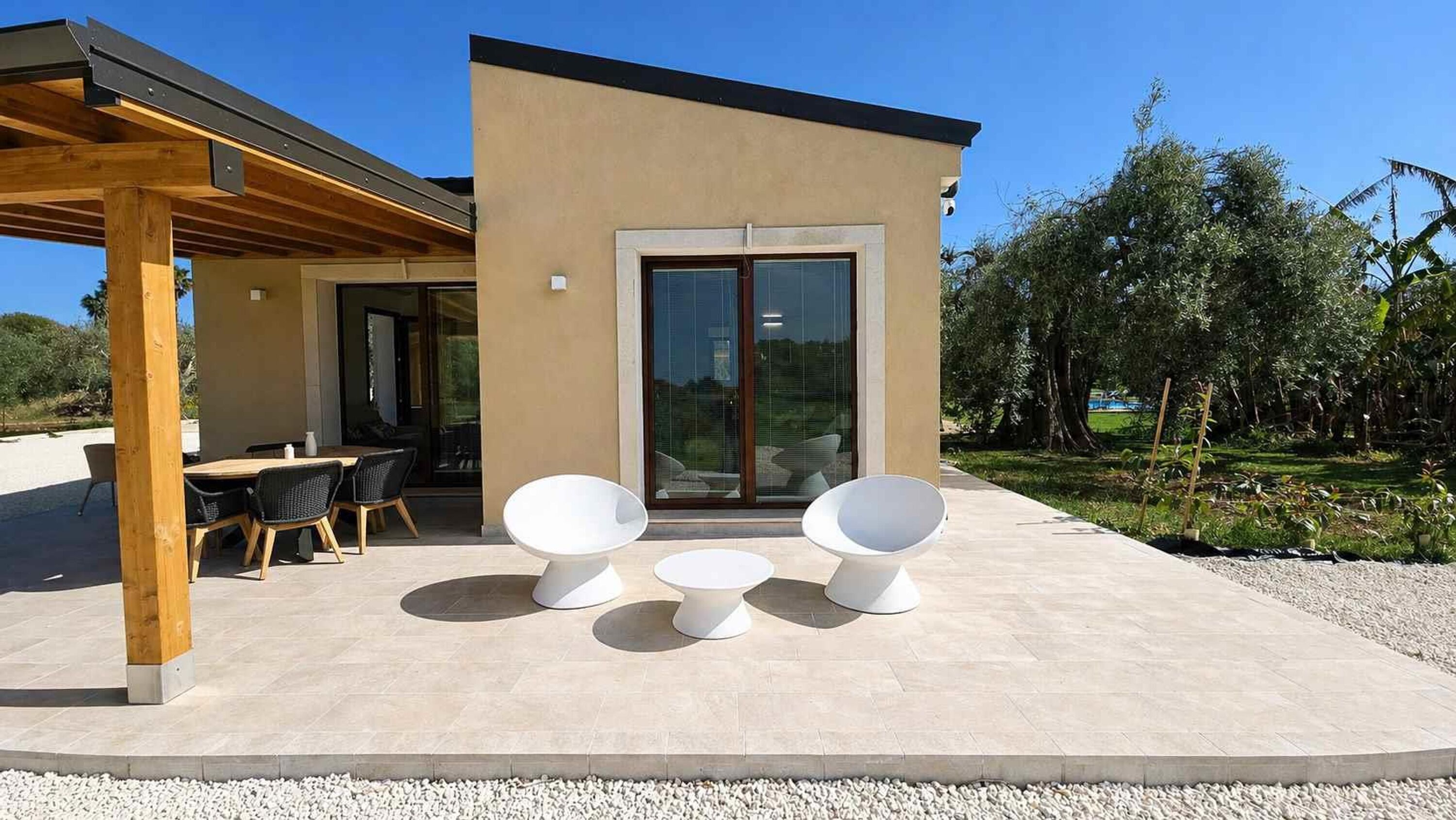 A modern house with a patio, outdoor seating, and a view of the surrounding garden.
