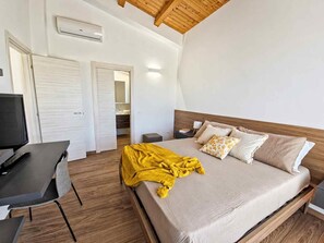Ein Schlafzimmer mit Bett, Nachttisch, Fernseher und Holzboden.
