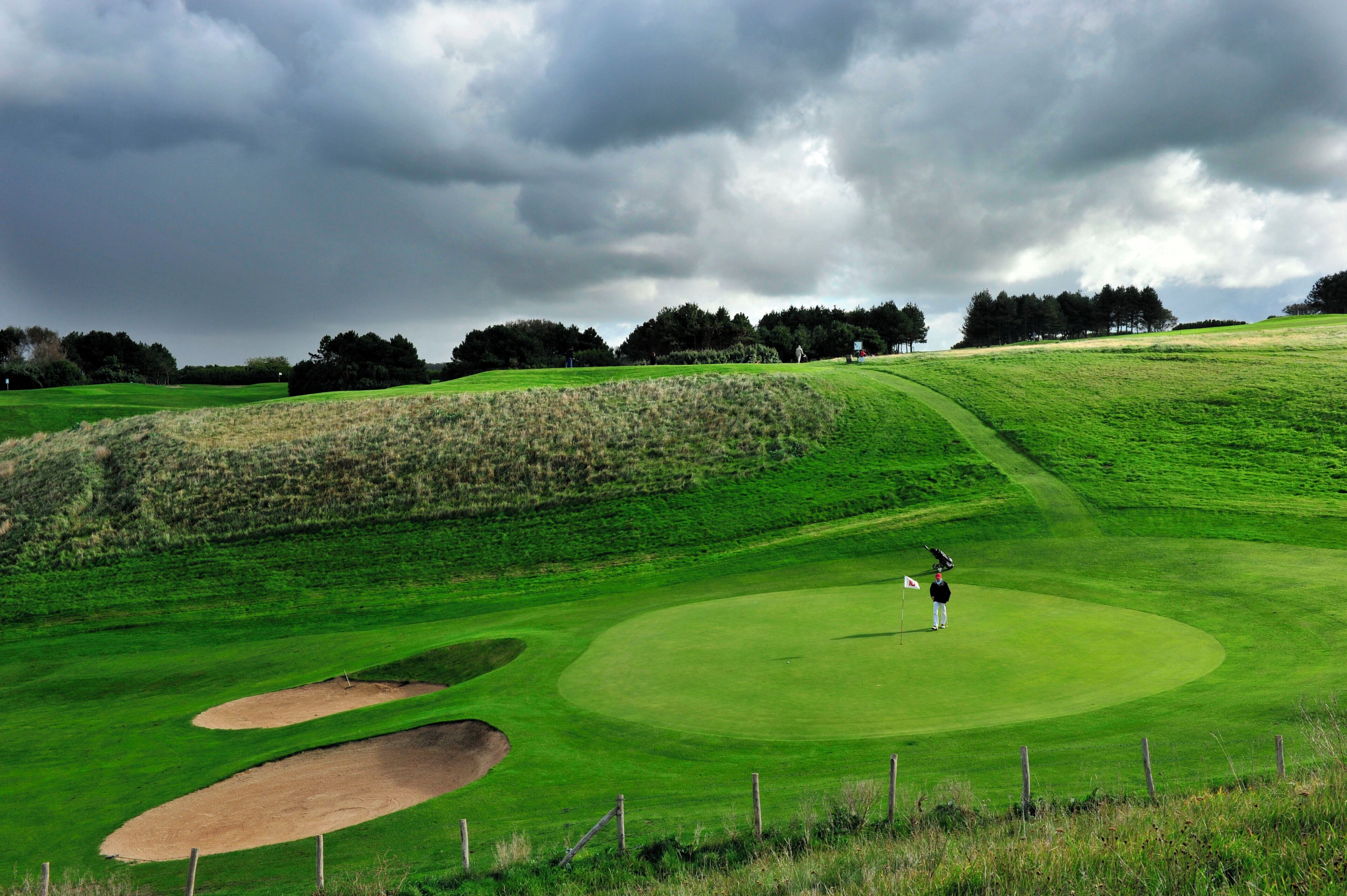 Un parcours de golf avec des bunkers, un mât de drapeau et un golfeur.