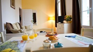 Hotellihuone, jossa on aamiaisella katettu ruokapöytä, sohva, televisio ja ikkuna, jossa on verhot.