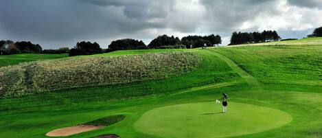 A golf course with bunkers, a flagstick, and a golfer.
