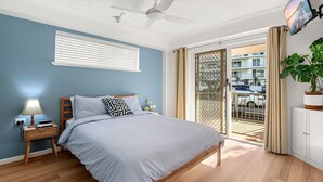 A bedroom with a bed, a nightstand, a lamp, a ceiling fan, a window with blinds, a sliding glass door, and a view of the outside. - Canberra Heights Unit 5, 35 Canberra Terrace, King (Kings Beach)