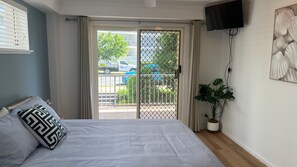 A bedroom with a bed, a TV, a window with curtains, and a plant. - Canberra Heights Unit 5, 35 Canberra Terrace, King (Kings Beach)