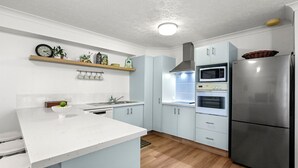 A modern kitchen with a white countertop, stainless steel appliances, and light blue cabinetry. - Canberra Heights Unit 5, 35 Canberra Terrace, King (Kings Beach)
