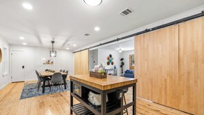 A modern dining area with a wooden table, chairs, and a kitchen island. - Girls Trip Getaway | Pool + Spa Near Main Street (Fredericksburg)