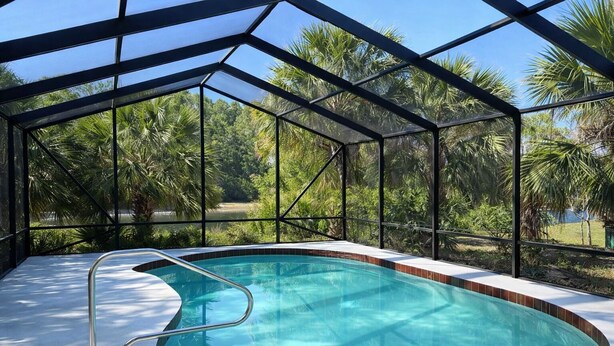 A swimming pool with a glass enclosure, surrounded by palm trees and a clear sky. - Heated pool home with a lake view! (St. Augustine)
