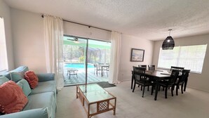 A living room with a sofa, coffee table, dining table, chairs, and a view of a swimming pool. - Heated pool home with a lake view! (St. Augustine)