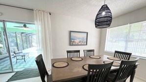 A dining room with a large table, six chairs, a hanging light fixture, and a painting on the wall. - Heated pool home with a lake view! (St. Augustine)