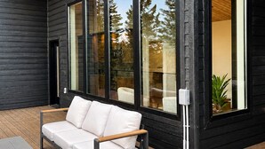 Ein moderner Außenbereich mit einer Sitzecke, einer Couch und einem Tisch, großen Fenstern und einer Holzbalkendecke.