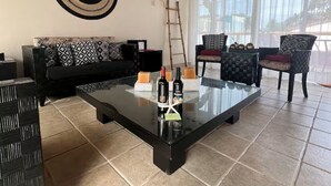 Un soggiorno con soffitto in legno, un divano nero, un tavolino da caffè in vetro e vista attraverso ampie finestre.