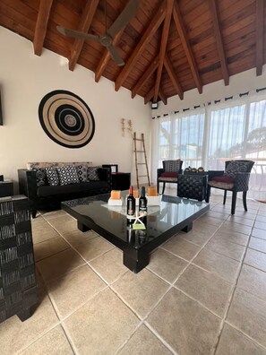 A living room with a wooden ceiling, a black sofa, a glass coffee table, and a view through large windows. - Casa Mariposas Ixtapa Pet Friendly Eco-Villa with Unlimited A/C and Solar Energy (Ixtapa Zihuatanejo)