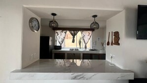 Una cucina con piano di lavoro in marmo, una sveglia, luci a sospensione e vista all'esterno.