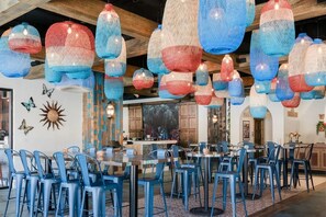 Restaurante con sillas azules, mesas y faroles rojos y azules colgando.