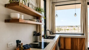 Uma cozinha moderna com prateleiras de madeira, bancada preta e janela com vista para uma paisagem desértica.