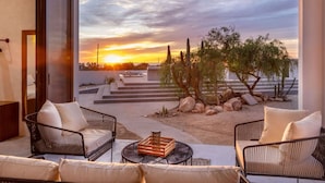 Uma área de estar moderna ao ar livre, com vista para um pôr do sol e paisagem desértica.
