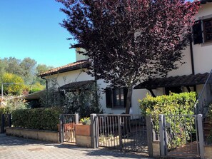 A house with a tiled roof, a garden with a metal gate, and a tree with red leaves. - Cozy Tuscan house in Florentine Chianti among vineyards, olive groves and cypress trees. (Varna)