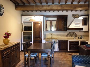 A kitchen with wooden cabinets, a dining table, and chairs. There is a vase with flowers on the counter. - Cozy Tuscan house in Florentine Chianti among vineyards, olive groves and cypress trees. (Varna)