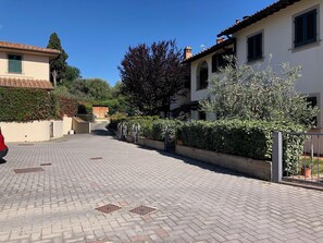 Ein gepflasterter Innenhof mit einem roten Auto auf der linken Seite, umgeben von Gebäuden mit Ziegeldächern und grünen Fensterläden.