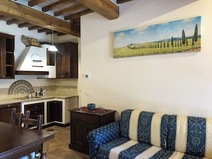 A dining area with a wooden table and chairs, a kitchen with dark wooden cabinets, and a blue patterned sofa. - Cozy Tuscan house in Florentine Chianti among vineyards, olive groves and cypress trees. (Varna)