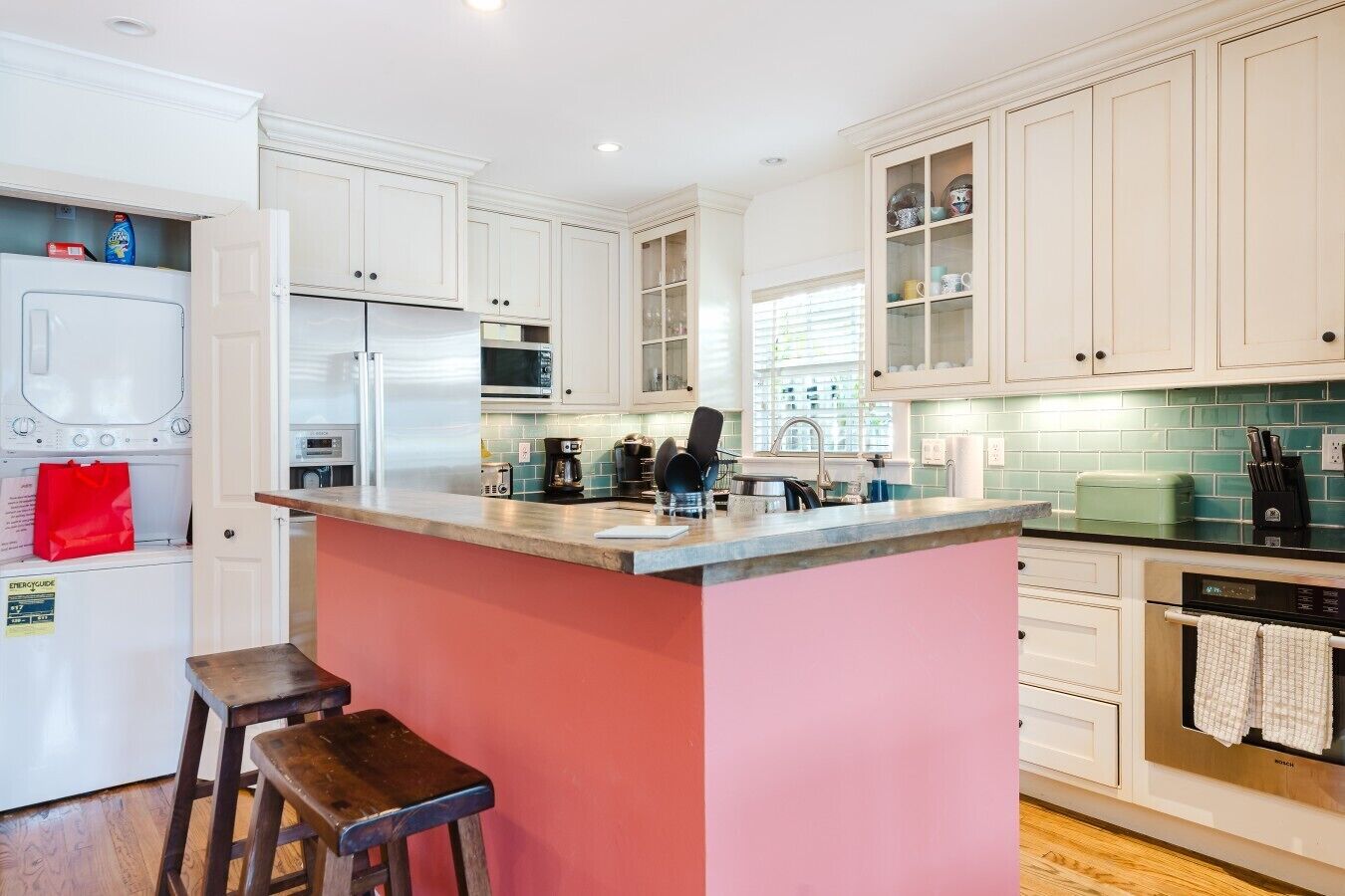 A kitchen with white cabinets, a pink island, a stainless steel refrigerator, a microwave, and a coffee maker.
