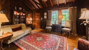 A cozy room with a wooden ceiling, a large rug, a sofa, two chairs, a bookshelf, and a window with curtains. - Palm Ridge House w/ Pool and Cabana Near Beach (West Palm Beach)
