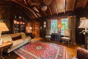 A cozy room with a wooden ceiling, a large rug, a sofa, two chairs, a bookshelf, and a window with curtains. - Palm Ridge House w/ Pool and Cabana Near Beach (West Palm Beach)