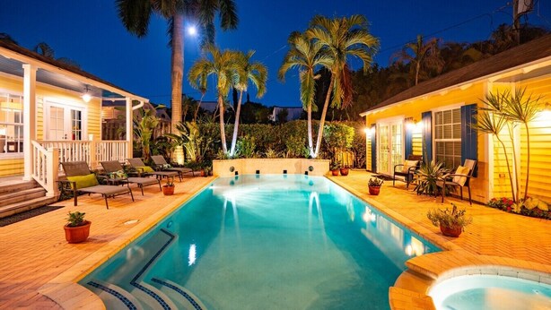 A swimming pool with a wooden deck, lounge chairs, and palm trees. - Palm Ridge House w/ Pool and Cabana Near Beach (West Palm Beach)