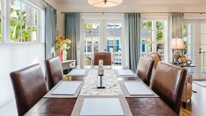 Comedor con una mesa grande, sillas de cuero, una araña y ventanas amplias con cortinas.