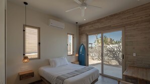 Une chambre à coucher avec un lit, une table de chevet, une lampe et une vue sur l’extérieur, accessible par une porte coulissante.
