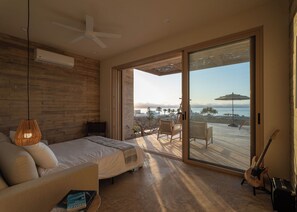 Ein Schlafzimmer mit einem Bett, einem Deckenventilator, einer großen Schiebeglasdoor, die auf einen Balkon mit Outdoor-Möbeln und einer Gitarre führt.