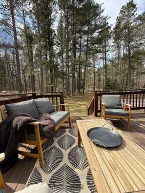 Eine Terrasse mit Gartenmöbeln, einem gemusterten Teppich und Blick auf einen Wald.