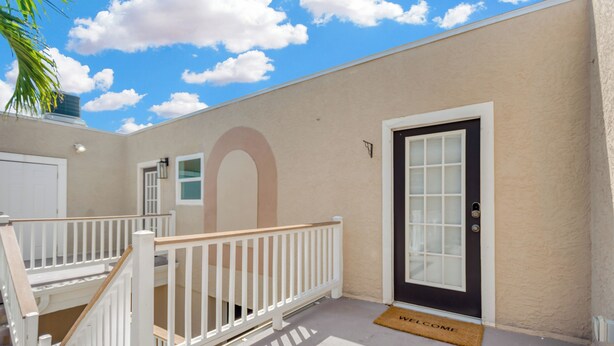 A building with a beige exterior, a black door with a glass panel, a white railing, and a welcome mat. - 1 Bedroom Studio in Waterfront Building with Dock Access (Treasure Island)