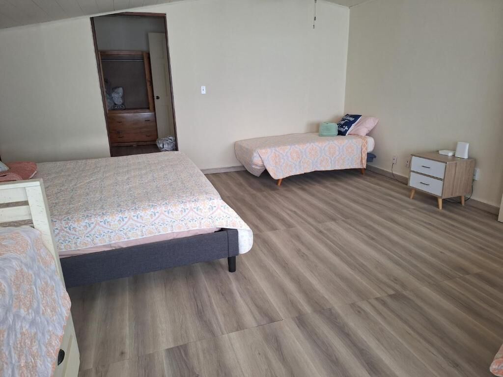 A bedroom with two beds, a wooden wardrobe, a small bedside table, and a door leading to another room.