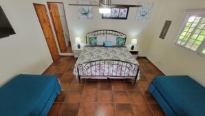 Un dormitorio con una cama, dos mesitas de noche con lámparas, un ventilador de techo, una ventana y una puerta.