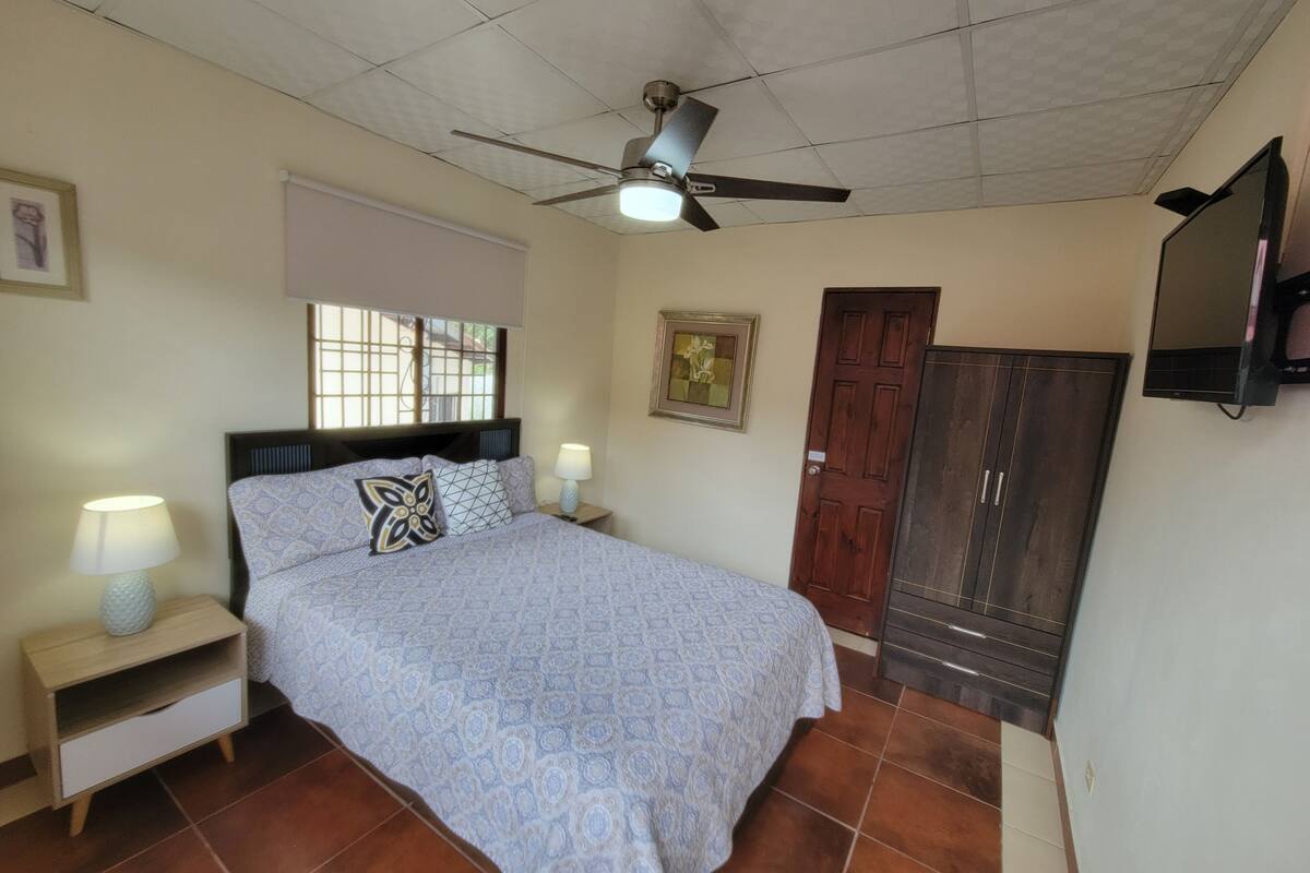 A bedroom with a bed, nightstands, a ceiling fan, a TV, a window, and a door.