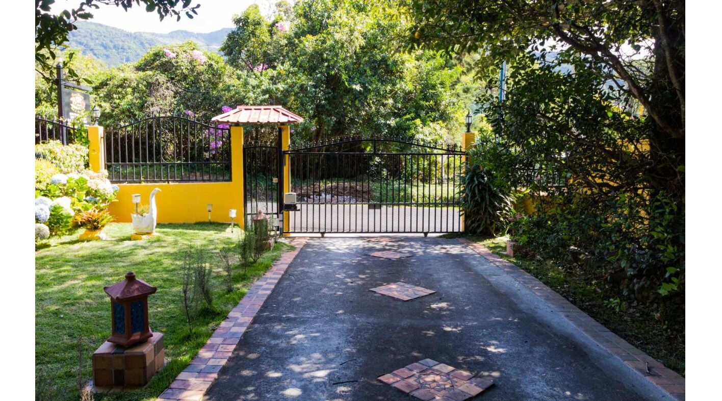 Una entrada protegida con un muro amarillo, una reja metálica y un camino pavimentado que conduce a una zona cubierta.