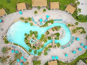 An aerial view of a resort with a large central swimming pool, multiple lounge areas, and palm trees. - 8BR family retreat w/ game room & pool (Four Corners)