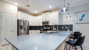 A modern kitchen with white cabinets, stainless steel appliances, a large island, and black bar stools. - 8BR family retreat w/ game room & pool (Four Corners)